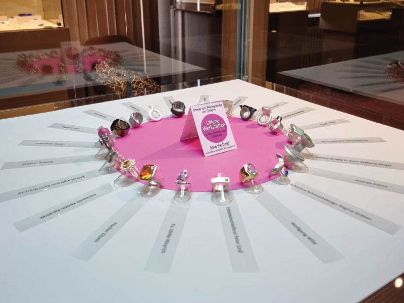 Eine Frauenhand greift in eine Auslage und berührt einen der 21 Ringe