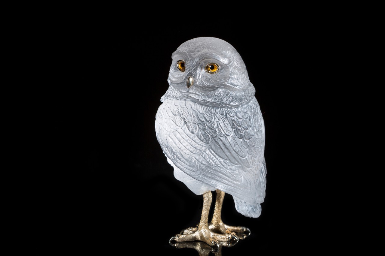 Auf dem Bild sieht man einen kleinen Kauz aus Bergkristall graviert, mit goldgefassten Augen, goldenem Schnabel und Krallen.