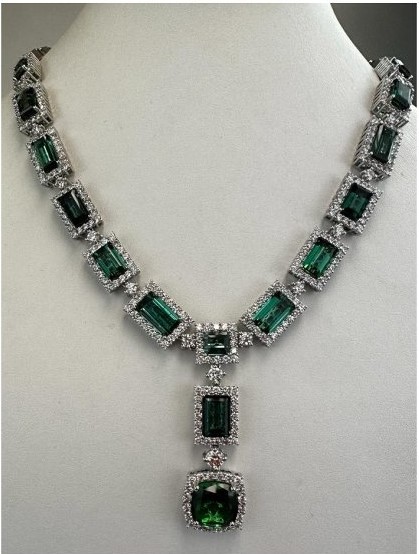Man sieht ein Collier mit rechteckigen facettierten grünen Turmalinen, jeweils umrahmt von Brillanten in Weißgold gefasst. In der Mitte ist ein Anhänger mit 2 weiteren größeren Turmalinen und Brillanten eingearbeitet.